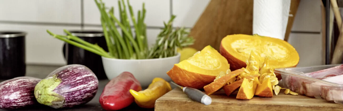 Das Bild zeigt ein Holzbrett, das in der Küche steht. Auf dem Brett liegt Obst und Gemüse.